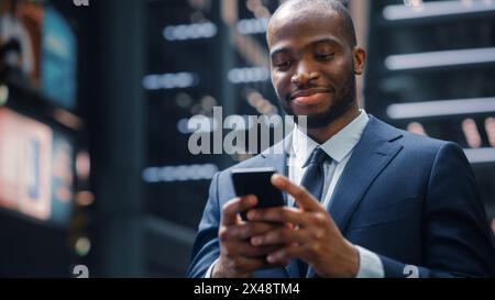 Ritratto di un uomo d'affari afroamericano di successo sulla strada del quartiere centrale degli affari di Big City. Black Digital Entrepreneur utilizza l'app per l'e-Commerce dei telefoni cellulari per gli investimenti nel mercato azionario Foto Stock