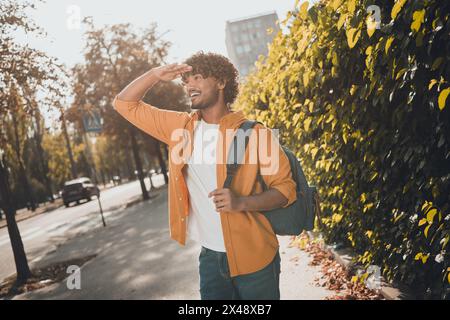 Foto di un allegro uomo latino vestito con abiti eleganti zaino che cammina in viaggio guardando l'architettura moderna del centro all'aperto Foto Stock