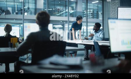 Diversi team di manager che lavorano e discutono nel moderno Big City Office. I colleghi lavorano su nuove opportunità di business, il CEO ha incontrato il dipendente e parla di investire nel futuro. Foto Stock