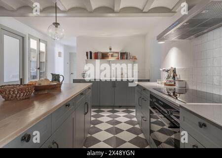 Una bella e spaziosa cucina in stile casa colonica con ripiano in marmo bianco, isola con ripiano in legno e armadietti Foto Stock