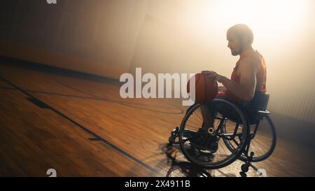 Il giocatore di pallacanestro su sedia a rotelle che indossa l'uniforme rossa porta la palla a segnare un gol perfetto. Determinazione, formazione, ispirazione di una persona con disabilità. Grandangolo con colori caldi Foto Stock