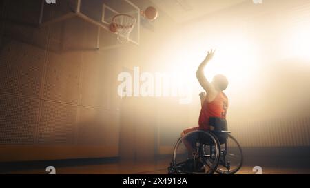 Giocatore di pallacanestro in sedia a rotelle che indossa la palla da tiro in uniforme rossa con successo, segnando un gol perfetto. Determinazione, formazione, ispirazione di una persona con disabilità. Grandangolo con colori caldi Foto Stock