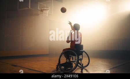 Giocatore di pallacanestro in sedia a rotelle che indossa la palla da tiro in uniforme rossa con successo, segnando un gol perfetto. Determinazione, formazione, ispirazione di una persona con disabilità. Grandangolo con colori caldi Foto Stock