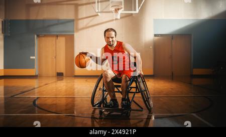 Ritratto di un bel giocatore di pallacanestro in sedia a rotelle che indossa la palla Dribbling della camicia rossa, guarda la fotocamera e sorride. Persona determinata e stimolata con disabilità gioca per vincere Foto Stock