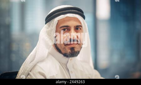 Ritratto di un uomo d'affari arabo di successo in abiti tradizionali che sorride dolcemente, indossando Kandura bianca e Agal nero, mantenendo un Ghutra in posizione. Arabia Saudita, Emirati, concetto di uomo d'affari arabo. Foto Stock