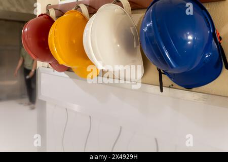 Caschi di sicurezza differenziati dal colore rosso, giallo, bianco e blu che sono appesi alla parete dell'ospedale Foto Stock