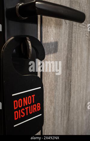 Cartello nero "non disturbare" con testo rosso appeso sulla chiave della porta nella camera dell'hotel Foto Stock