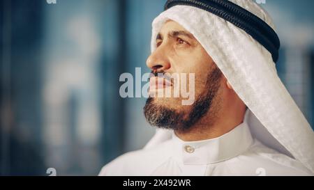 Ritratto di un uomo d'affari musulmano di successo in abiti tradizionali che sorride dolcemente, indossando Kandura bianca e Agal nera, mantenendo un Ghutra in posizione. Arabia Saudita, Emirati, concetto di uomo d'affari arabo. Foto Stock