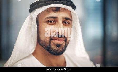 Ritratto di un uomo d'affari arabo di successo in abiti tradizionali che sorride dolcemente, indossando Kandura bianca e Agal nero, mantenendo un Ghutra in posizione. Arabia Saudita, Emirati, concetto di uomo d'affari arabo. Foto Stock