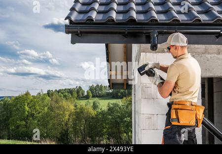 Appaltatore edile operaio sul tetto che installa grondaie per la casa. Tema del cantiere. Foto Stock