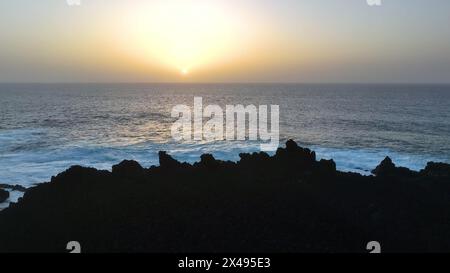 Vista aerea 4K al rallentatore dell'oceano azzurro e delle onde giganti che si infrangono sulla scogliera rocciosa con spruzzi e schiuma bianca. Lanzarote. Isole Canarie, Spagna Foto Stock