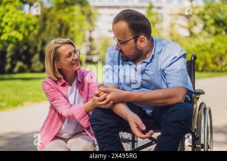 L'uomo in sedia a rotelle sta trascorrendo del tempo con il suo amico nel parco. Foto Stock