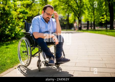 Ritratto dell'uomo felice in sedia a rotelle. Si sta godendo una giornata di sole nel parco cittadino. Foto Stock