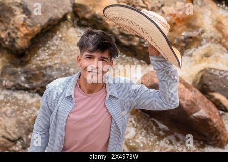 stile di vita. Foto ritratto di un giovane indiano con un cappello in mano accanto al fiume Foto Stock