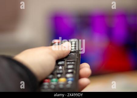 Una mano regge un telecomando davanti a un televisore, un gadget utilizzato per controllare apparecchiature elettroniche come dispositivi audio e video Foto Stock