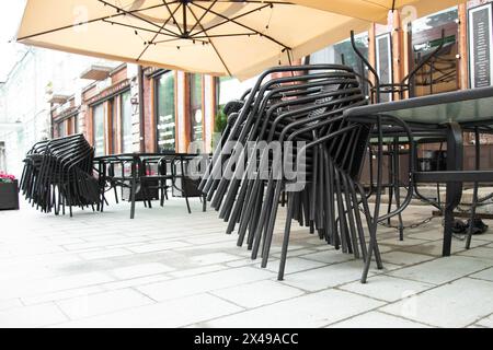 Caffetteria all'aperto chiusa. Sedie impilate vicino ai tavoli da caffè in piedi sulla strada Foto Stock