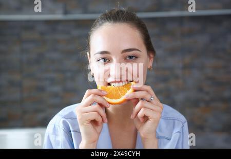 Bella bruna donna sorridente mangiare crudo affettato gustosi mezza arancia in cucina di mattina ritratto. La perdita di peso beauty fit concept Foto Stock