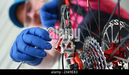 Uomo addetto alla riparazione del servizio biciclette con guanti protettivi blu adatta la moto per prepararsi al primo piano del concetto stagionale Foto Stock