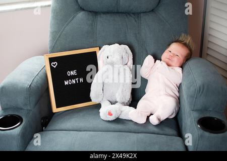 Bimba caucasica di un mese vicino al peluche e al tabellone. Foto mensile del neonato Foto Stock