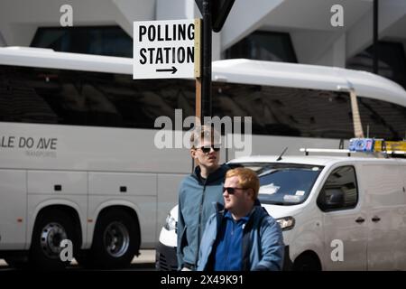 La gente cammina accanto a un cartello che indica un posto elettorale in vista delle elezioni locali di domani a Westminster, Londra. Domani si terranno le elezioni locali in varie parti del Regno Unito, in cui si prevede che il partito conservatore al governo subirà un gran numero di perdite. Foto Stock