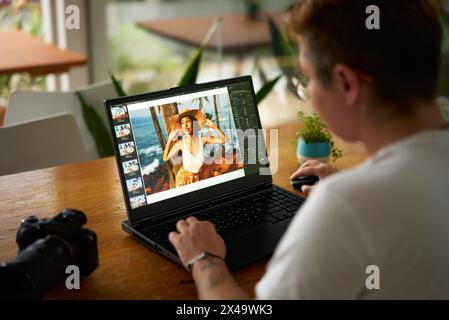 Il fotografo modifica la foto del modello sul computer portatile al tavolo del bar. Il freelance lavora sull'elaborazione delle immagini, utilizza software di editing nello spazio pubblico. Creatività Foto Stock