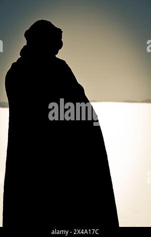 Una persona che indossa un mantello nero e un copricapo turbante nero contempla la vista delle dune di gesso tra il cielo al White Sands NP di Alamogordo, NEW MEXICO Foto Stock