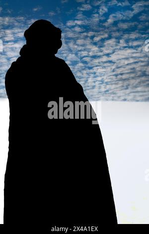 Una persona che indossa un mantello nero e un copricapo turbante nero contempla la vista delle dune di gesso tra il cielo al White Sands NP di Alamogordo, NEW MEXICO Foto Stock