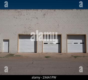 trascurato e datato ma funzionale decadimento urbano commerciale con atmosfera di metà secolo, tre porte bianche del garage in un edificio in mattoni bianchi con porta Foto Stock