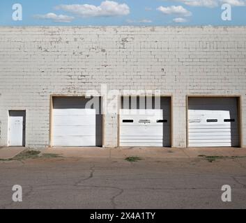 trascurato e datato ma funzionale decadimento urbano commerciale con atmosfera di metà secolo, tre porte bianche del garage in un edificio in mattoni bianchi con porta Foto Stock