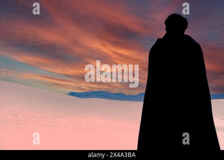 Una persona che indossa un mantello nero e un copricapo turbante nero contempla la vista delle dune di gesso tra il cielo al White Sands NP di Alamogordo, NEW MEXICO Foto Stock