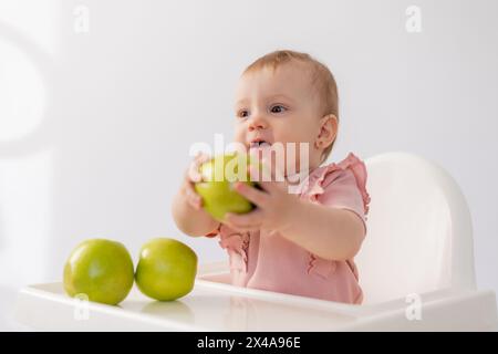 Un bambino carino in una sedia per bambini stuzzica le mele su sfondo bianco. Foto di alta qualità Foto Stock