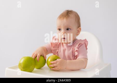 Un bambino carino in una sedia per bambini stuzzica le mele su sfondo bianco. Foto di alta qualità Foto Stock