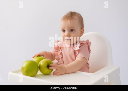 Un bambino carino in una sedia per bambini stuzzica le mele su sfondo bianco. Foto di alta qualità Foto Stock