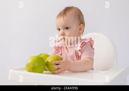 Un bambino carino in una sedia per bambini stuzzica le mele su sfondo bianco. Foto di alta qualità Foto Stock