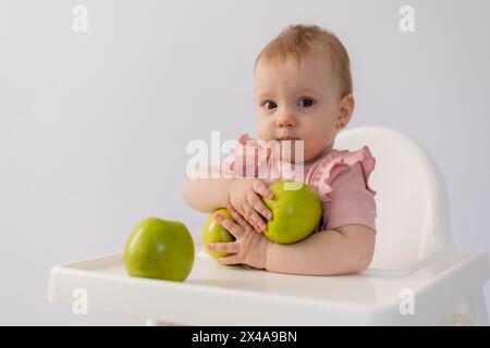 Un bambino carino in una sedia per bambini stuzzica le mele su sfondo bianco. Foto di alta qualità Foto Stock