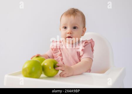 Un bambino carino in una sedia per bambini stuzzica le mele su sfondo bianco. Foto di alta qualità Foto Stock