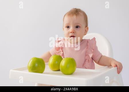 Un bambino carino in una sedia per bambini stuzzica le mele su sfondo bianco. Foto di alta qualità Foto Stock