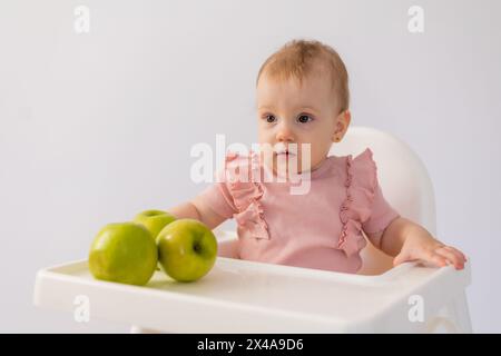 Un bambino carino in una sedia per bambini stuzzica le mele su sfondo bianco. Foto di alta qualità Foto Stock