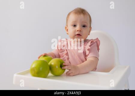 Un bambino carino in una sedia per bambini stuzzica le mele su sfondo bianco. Foto di alta qualità Foto Stock