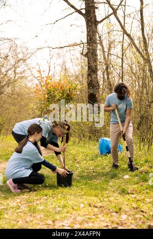 Gruppo di attivisti che piantano piccoli alberi per la conservazione della natura, contribuendo alla sostenibilità e alla conservazione dell'ecosistema. Volontari che uniscono le mani per la cura dell'ambiente, scavando buchi per i semi. Foto Stock