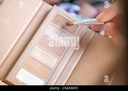 Dettaglio della mano di una donna che prende un po' di trucco da una tavolozza di trucco con tonalità marroni e dorate Foto Stock