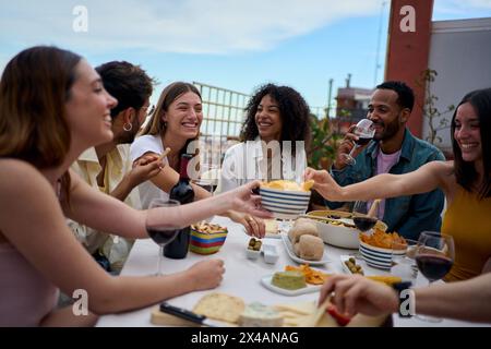Gruppo di giovani amici multietnici che gusteranno il pasto riuniti sul tetto Foto Stock