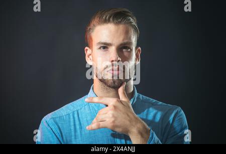 Uomo attento e non rasato in camicia in denim con mento a mano per prendere decisioni senza dubbio. Un uomo serio con la barba che pensa al futuro, alla pianificazione Foto Stock