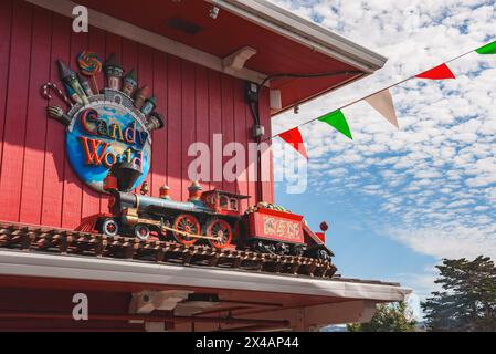 Colorata facciata del Candy World con locomotiva, ruote arancioni e bandiere festose nel parco divertimenti. Foto Stock