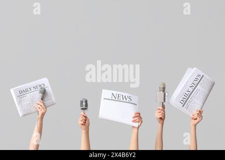 Mani femminili con giornali e microfoni su sfondo grigio Foto Stock