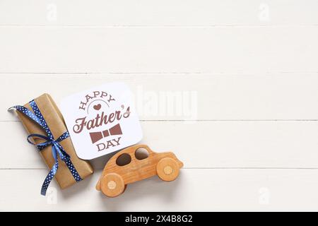 Confezione regalo, auto in legno e biglietto di auguri con testo "HAPPY FATHER'S DAY" su sfondo bianco in legno. Vista dall'alto Foto Stock