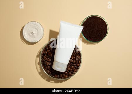 Vista dall'alto di un tubo di plastica bianco vuoto esposto su piatti Petri di chicchi di caffè decorati con un piatto Petri dalla consistenza crema su sfondo beige. Cen Foto Stock