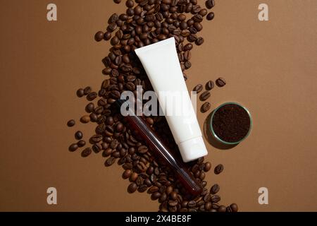 Tubo di plastica bianco con crema idratante per il viso, detergente per il viso o maschera visualizzato su sfondo marrone con chicchi di caffè e bicchieri. Vista dall'alto, perché Foto Stock