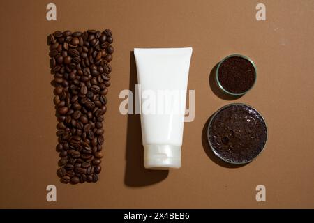 Vista dall'alto della provetta di plastica bianca senza etichetta visualizzata con chicchi di caffè e piastra Petri riempita con fondi di caffè su sfondo marrone. Scena di mockup per un Foto Stock