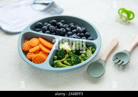 Ciotola in plastica per bambini con broccoli, mirtilli e carote. Alimenti sani per bambini nel recipiente Foto Stock